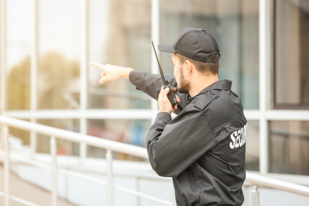 Male security guard using portable radio transmitter near building outdoors Male security guard using portable radio transmitter near building outdoors