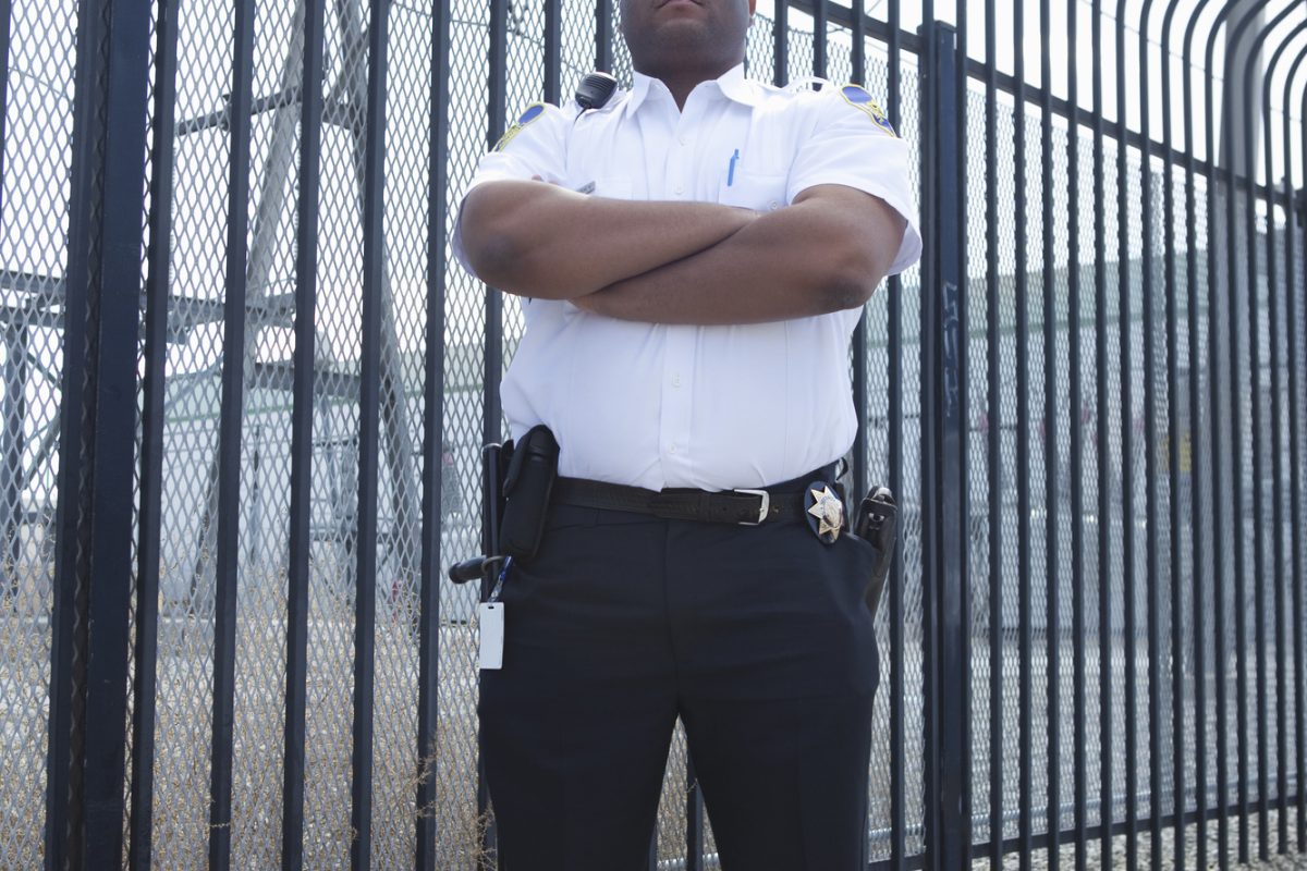 Confident security guard standing with arms crossed in front of the prison fence Full length of a confident security guard standing with arms crossed in front of the prison fence